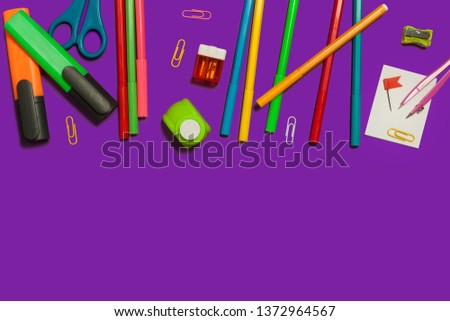 row of various school and office supplies lying on a purple background. free space for advertising text