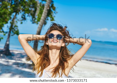 A red-haired woman with glasses tilted her head back and stands on the sand near the ocean                       