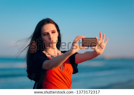 Female Tourist Taking Selfies at Sunset by the Sea. Woman taking pictures of herself at the beach in summer holiday
