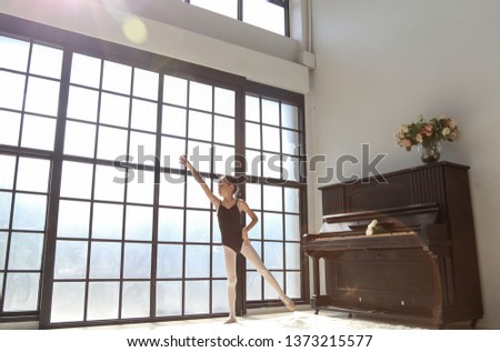 Cute ballerina little girl in black suit  dance practice in the room with old piano, kid ballet concept.