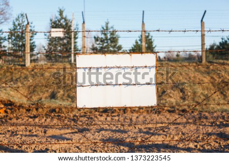 Barbed wire fence protects the danger zone. White sign board.