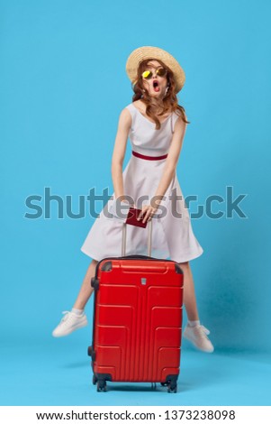 Pretty woman in a hat with a red suitcase and plane tickets blue background