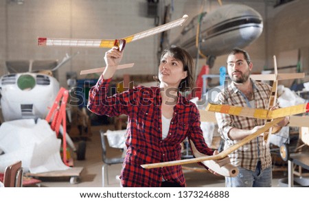 Portrait of positive couple having fun with light plane models in aircraft hangar