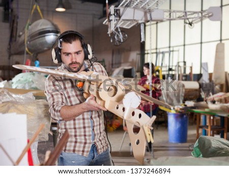 Young handsome bearded man enjoying his hobby - modeling light airplanes in aircraft hangar

