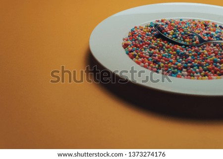 White plate and spoon with color preparations (vitamins, dyes, flavor enhancers, nutritional supplements, innovative technologies, candy sweets) on an orange background.