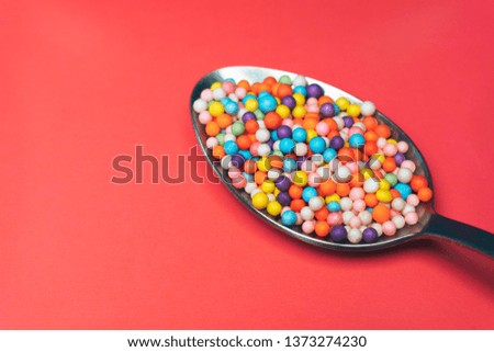 spoon colored preparations (vitamins, dyes, flavor enhancers, nutritional supplements, innovative technology, candy sweets) on a red background.