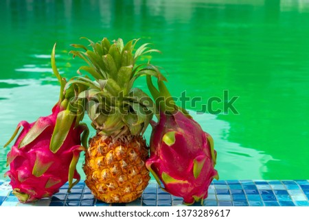 Ripe two dragon fruit and pineapple by the pool / Exotic fruit against the background of the pool on a sunny day