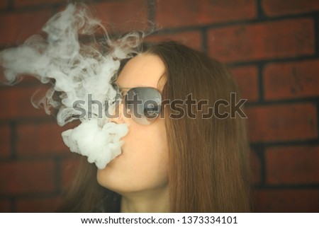 Vape teenager with  problem skin. Portrait of young cute girl in sunglasses smoking an electronic cigarette in the bar. Bad habit that is harmful to health. Vaping activity.