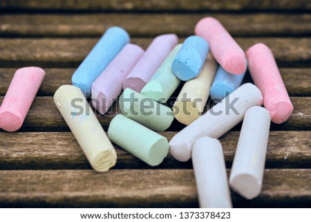A pile of bright colorful children's street chalk on the dark wooden bars of a bench on a playground. Seen in Nuremberg, Germany, April 2019