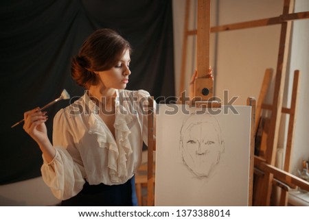 Female painter with brush standing against easel