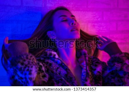 Fashion model brunette woman in colourful bright sparkles and neon lights posing in studio, portrait of beautiful girl, Vivid neon red-blue makeup,trendy glowing make-up. Art design colorful make up.