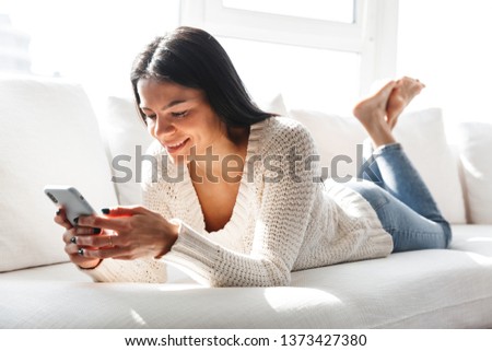 Lovely young woman relaxing on a couch at home, using mobile phone