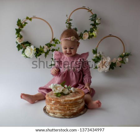Smash cake. One year old girl celebrates her birthday. Cake. Floral decor on a white background. Cute girl in a pink dress eats a cake.