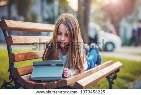 Good mood in the city park. Little girl enjoying in the park while searching internet with tablet. Education, lifestyle, technology concept