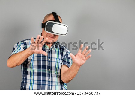 Grandfather looks into VR glasses, hand gestures, on a gray background