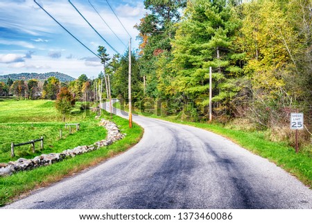 A rural road by farm land within the new england town of cornwall connecticut on a blue sky day.