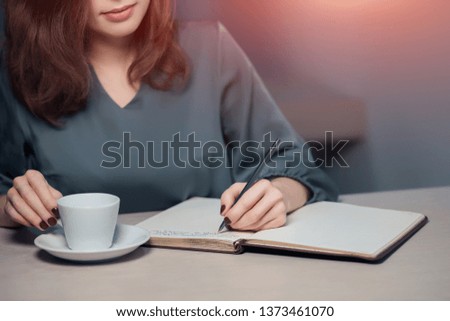 attractive woman has a cup of tea in restaurant and making notes in pad; writer makes a novel; poet writes a poem;