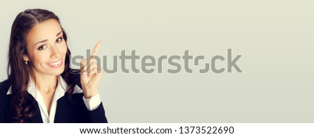 Picture of smiling young businesswoman showing blank area or empty copy space place for some text, advertising or slogan, over grey background. Business concept photo.
