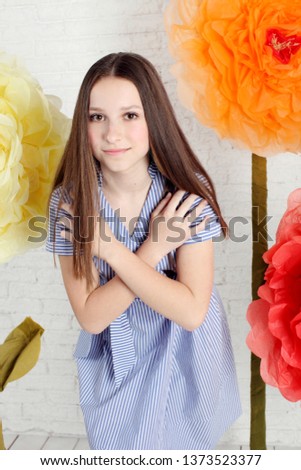 Beautiful teen girl posing in studio with artificial big flowers