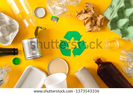 Environmental conservation concept - garbage prepared for recycling, cardboard, plastic, metal, glass, recycling sign, yellow background
