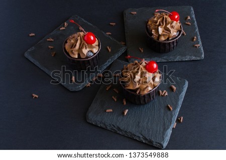 Chocolate cupcakes with chocolate cream decorated with cocktail cherry on black background