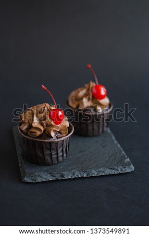 Chocolate cupcakes with chocolate cream decorated with cocktail cherry on black background