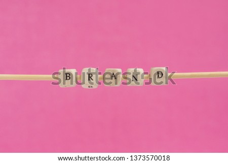 BRAND Word Written In Wooden Cube. Cube with letters isolated on pink background unfinished on a wooden stick hanging in the air, sign with wooden cubes