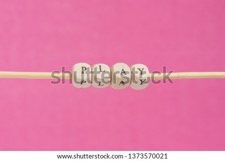 PLAY Word Written In Wooden Cube. Cube with letters isolated on pink background unfinished on a wooden stick hanging in the air, sign with wooden cubes