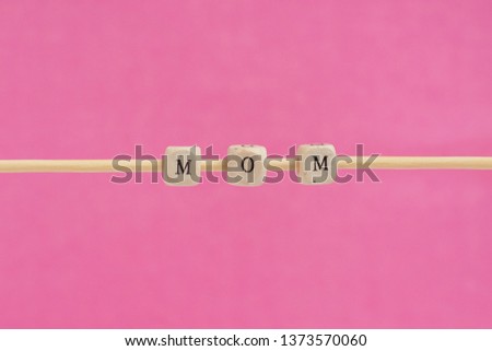 MOM Word Written In Wooden Cube. Cube with letters isolated on pink background unfinished on a wooden stick hanging in the air, sign with wooden cubes