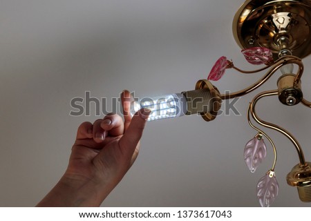 female hand inserts a light bulb into the threaded socket. she is shining. Installation of household LED lamps of corn type, in the lamp holder, there is a toning.