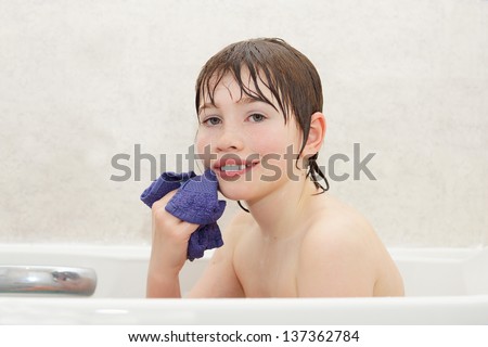 Healthy looking boy washing face with a wash cloth in the bath tub