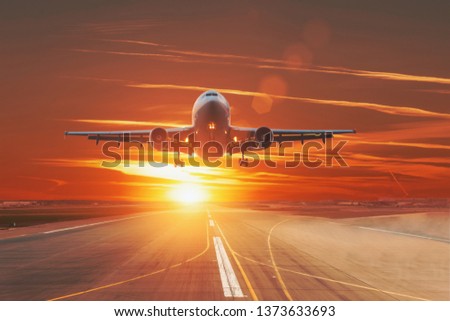 Commercial jet airplane flying over runway dramatic sunset sky