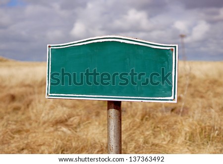 Old sign post, with blank space for own message, against    meadow grass and cloudy sky
