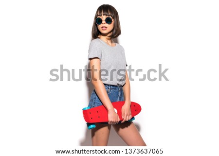 Portrait of cheerful woman in sunglasses posing with skateboard while standing isolated over white background