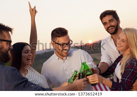 Group of friends at a summertime outdoor party having fun, dancing, drinking beer and making a toast
