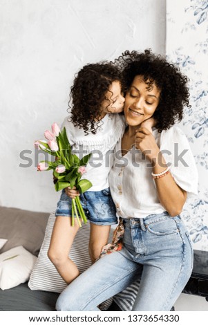 Mom and little cute curly girl spend time together, hugging and kissing each other.
