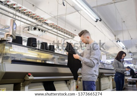 close up photo of a young man analyzing a piece of clothes and a woman working on industrial knitting machine