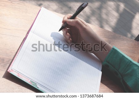 partial view of of female hand holding pen over notebook with copy space on wooden table in coffee shop
