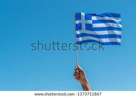 Flag of Greece in human hand on sky background.