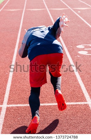 A high school sprinter is practicing the start of his race in the winter on a track. Picture taken from behind the athlete.