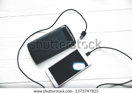 Black power bank with usb and smartphone on wooden background. Modern information technology photo.