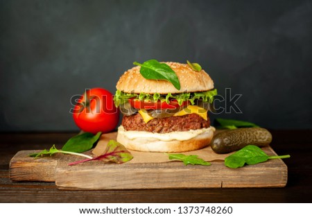 
Homemade hamburger with lettuce, tomato, cheese and cucumber on a cutting board