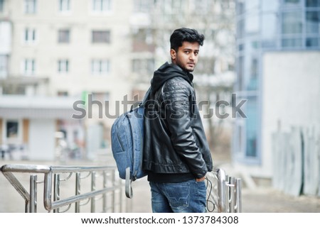 Stylish and casual asian man in black leather jacket with backpack posed at street.