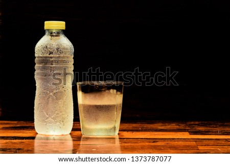 A​ bright​ glass​ and​ a​ bottle​ of​ cold​ water​ are​ on​ the​ wooden​ table background black.