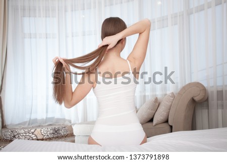 Young pretty woman stretching and do morning work-out on big bed at home. Woman in white Panties and T-shirt. Smiling and happy person in hotel room. 