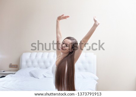 Young pretty woman stretching and do morning work-out on big bed at home. Woman in white Panties and T-shirt. Smiling and happy person in hotel room. 