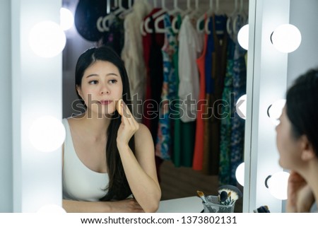 Young korean actress woman applying blush on her face with powder puff looking mirror with bulbs in dressing room. skin care concept. asian entertainer in backstage preparing for performance makeup