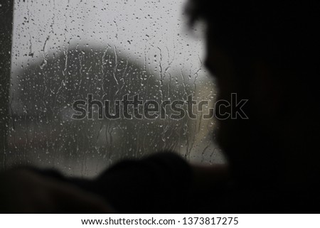 silhouette of a man sitting in the window with rain in mood of sadness and depression
