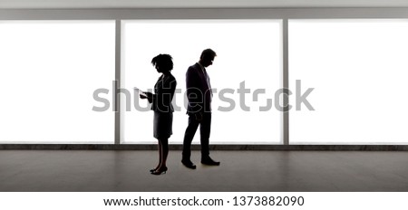 Silhouettes of a caucasian businessman and a black african american businesswoman discussing a business plan.  They are partners of a startup company.