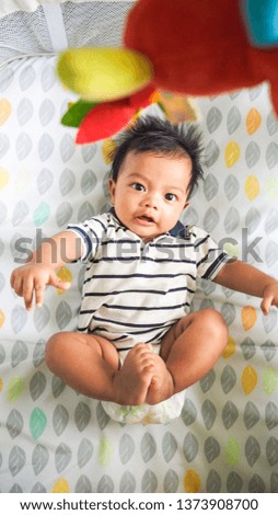 Adorable newborn baby playing on colorful toys. Close up baby picture try to play and grab toys. Child development. Asian boy. 